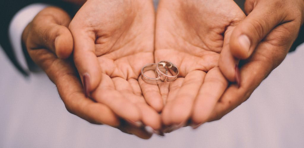 A bride and groom holding out their hands showing their wedding rings up close