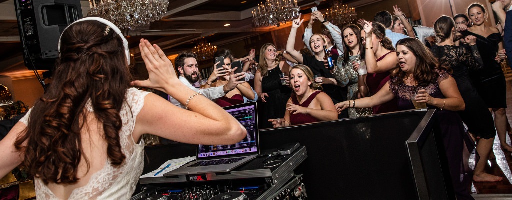 A bride playing wedding DJ at the reception as the guests cheer her on