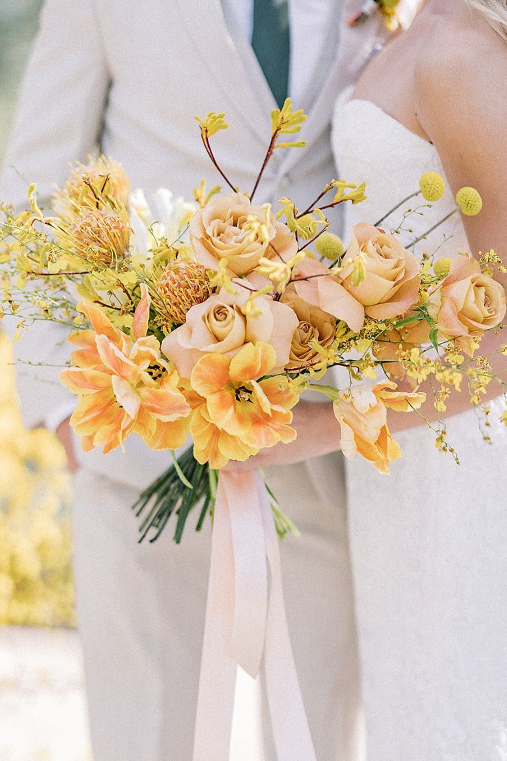 A beautiful yellow wedding bouquet being held by the bride