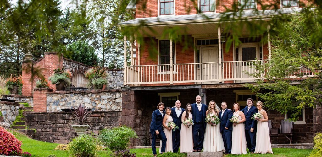 A wedding party posing in front of an old farmhouse