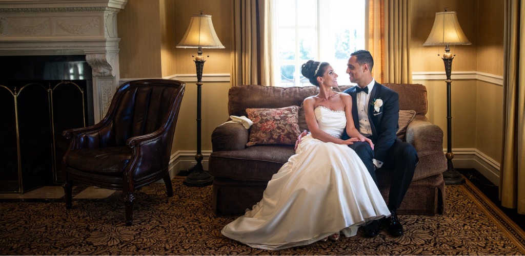 A bride and groom sitting on a couch smiling at each other. This is for the blog post called 6 month wedding planning timeline