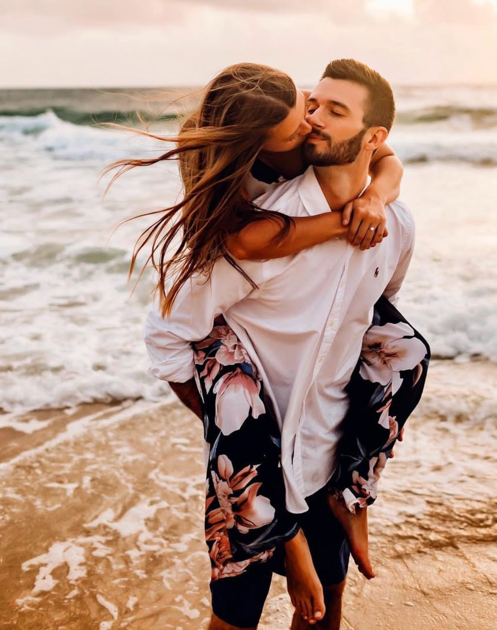 A couple posing for engagement photos at the beach. The girl is getting a piggyback ride from the guy