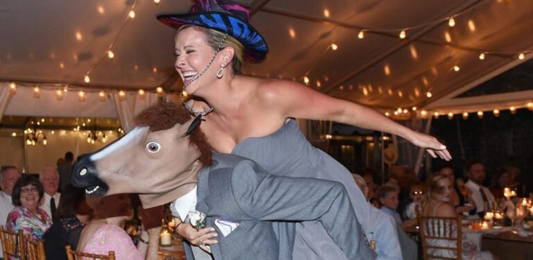 A brest man in a horse mask a maid of honor in a cowboy hat entering the wedding reception piggyback style. This is for the blog post called country wedding party entrance songs for wedding