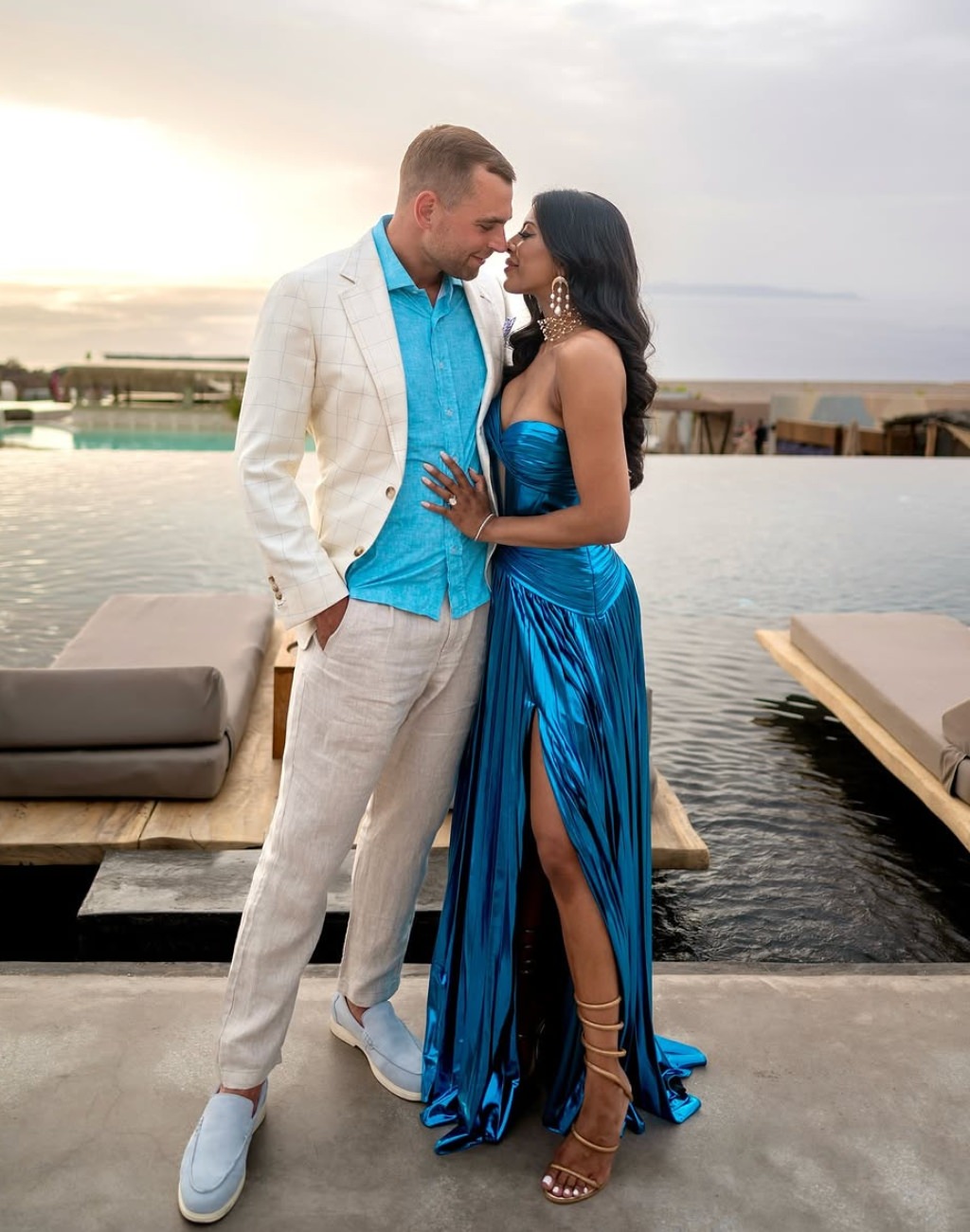 A man and woman posing for an engagement photo on a dock. The girl is wearing a bright blue dress.