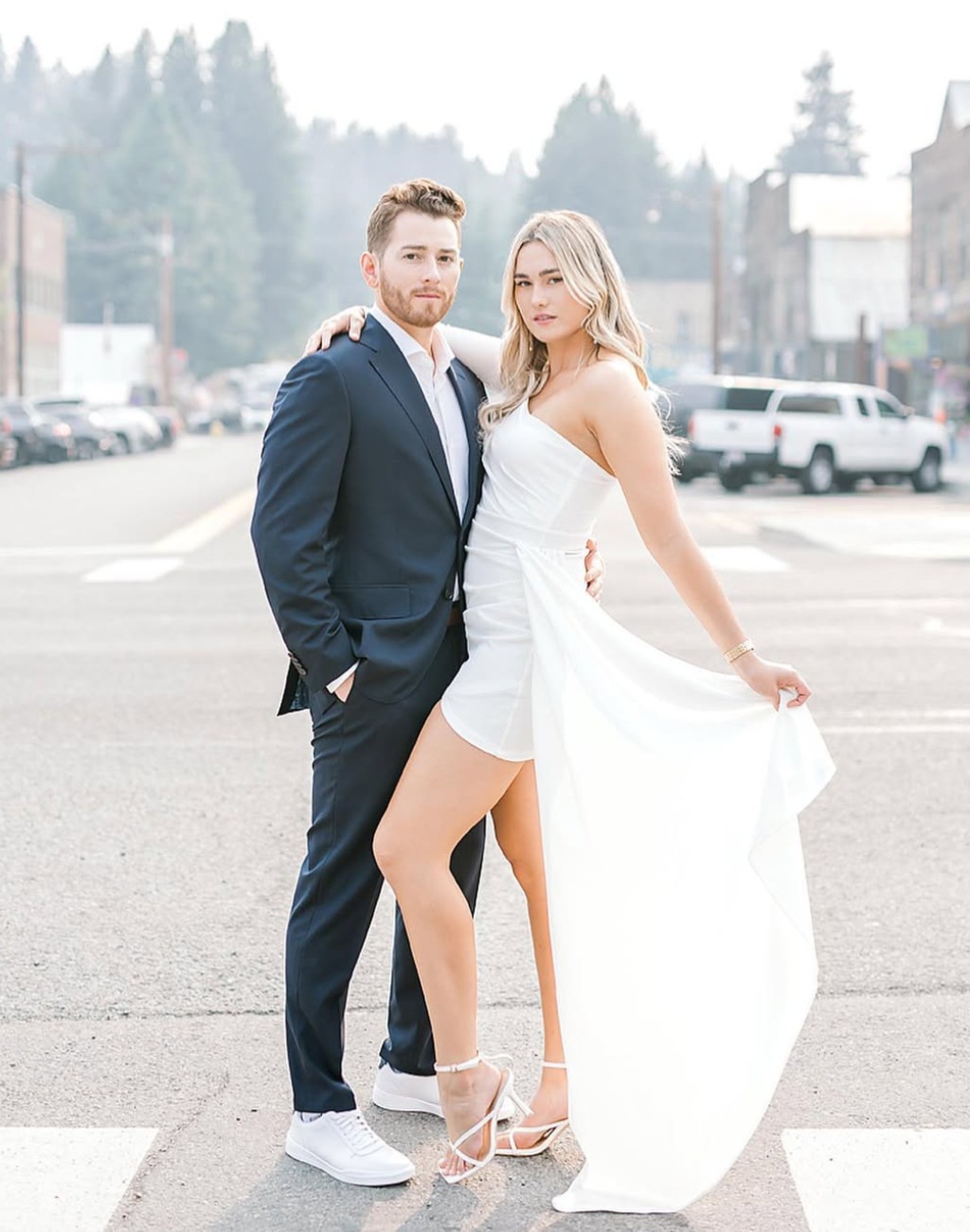 An engagement photo taken in the street with the girl wearing a white dress with white cape and the guy wearing a black suit and white shirt