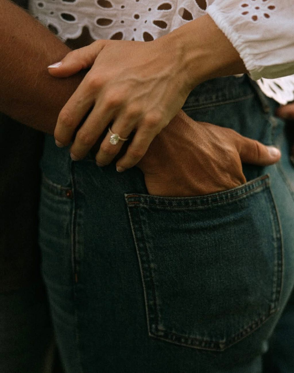 An engagement photo pose that shows a close up the guy's hand in the girl's back pocket and she is holding his wrist so you can see her engagement ring up close.