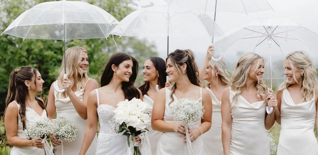 A bride and bridesmaids walking in the rain with umbrellas