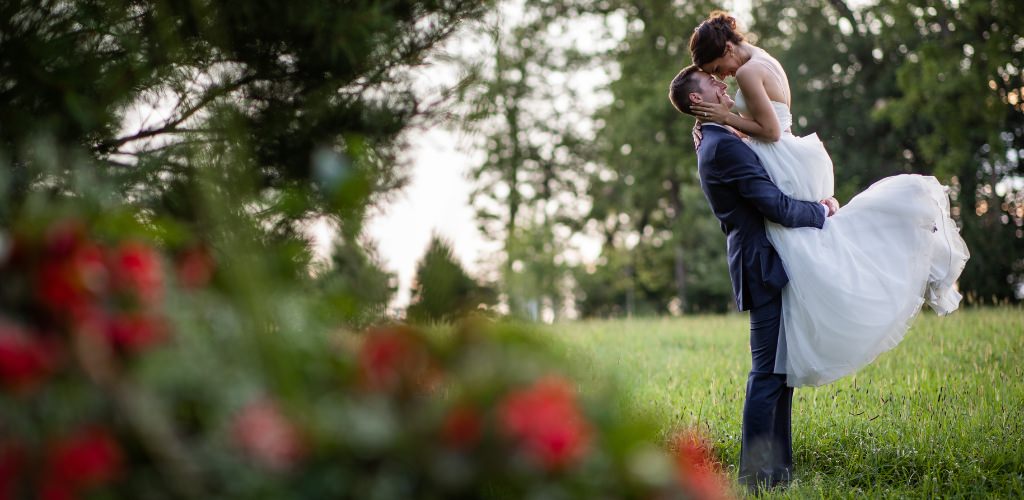 A groom picking up the bride and kissing her in a grass field with red flowers
