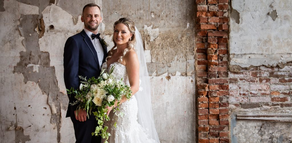 A bride and groom posing indoors in a room that has unfinished walls