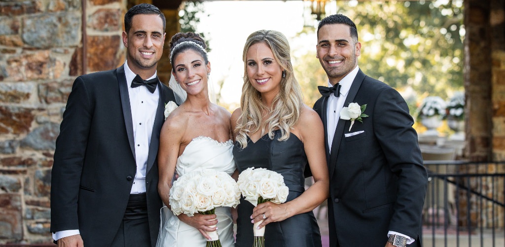 A small wedding party with only the bride, groom, best man, and maid of honor posing for a photo in all black and white attire