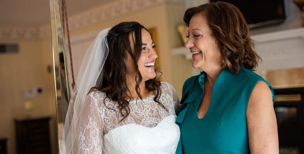 A bride and the mother of the bride smiling at each other on the wedding day