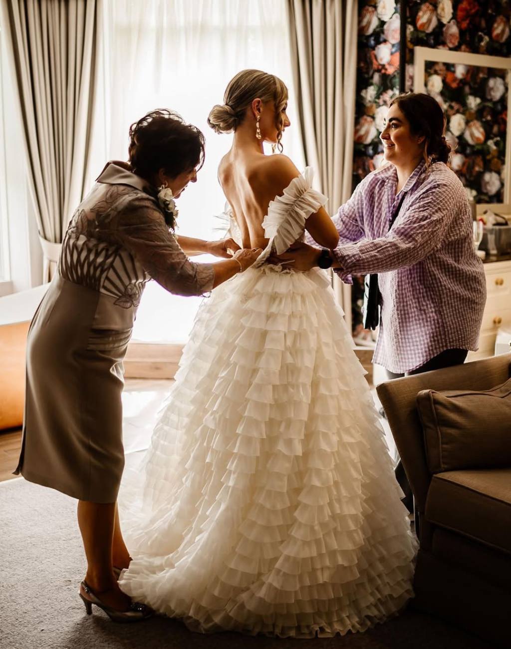 A bride's mom zipping up the bride's wedding dress with another family member helping