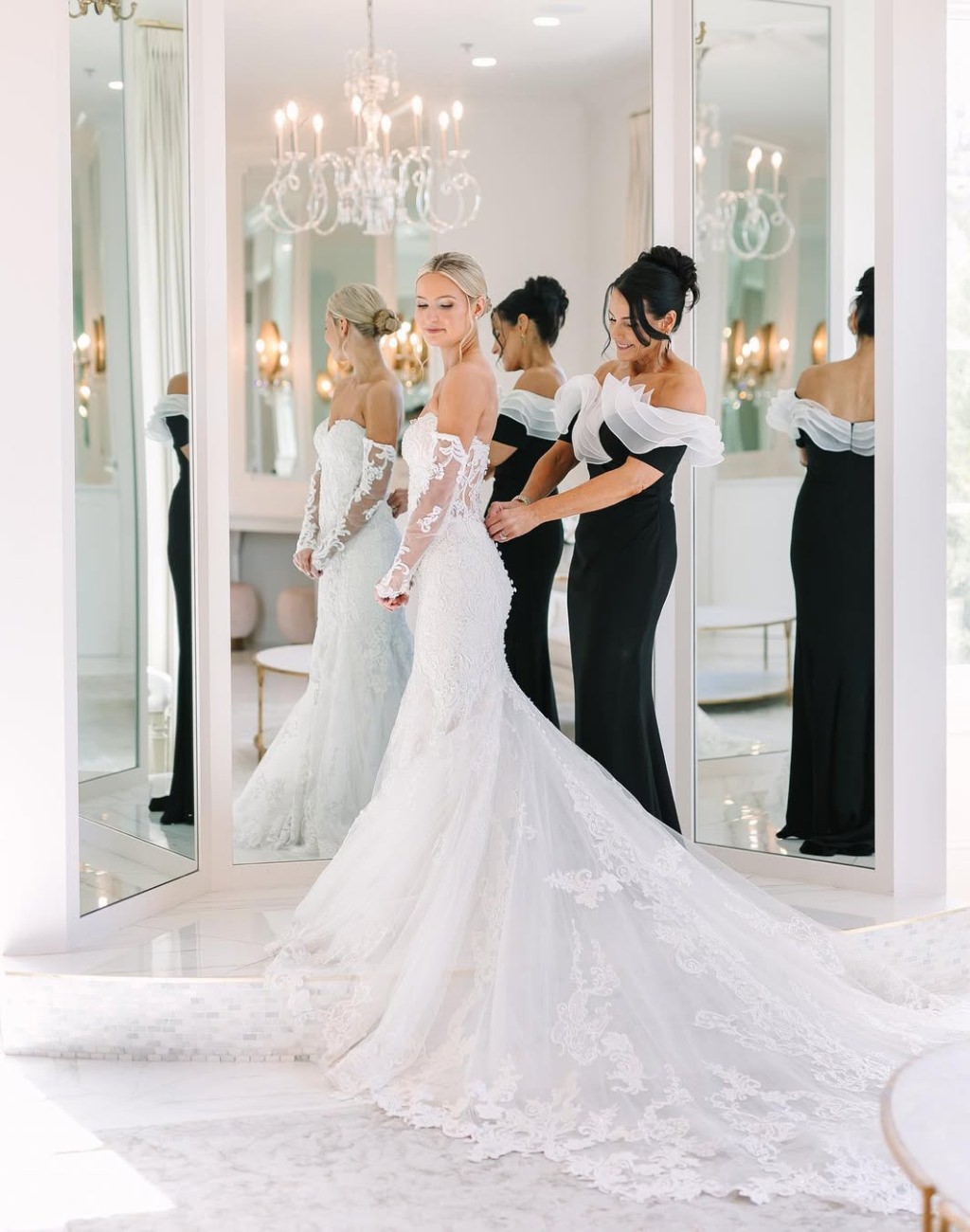 A bride's mom zipping up the bride's wedding dress in front of a huge mirror