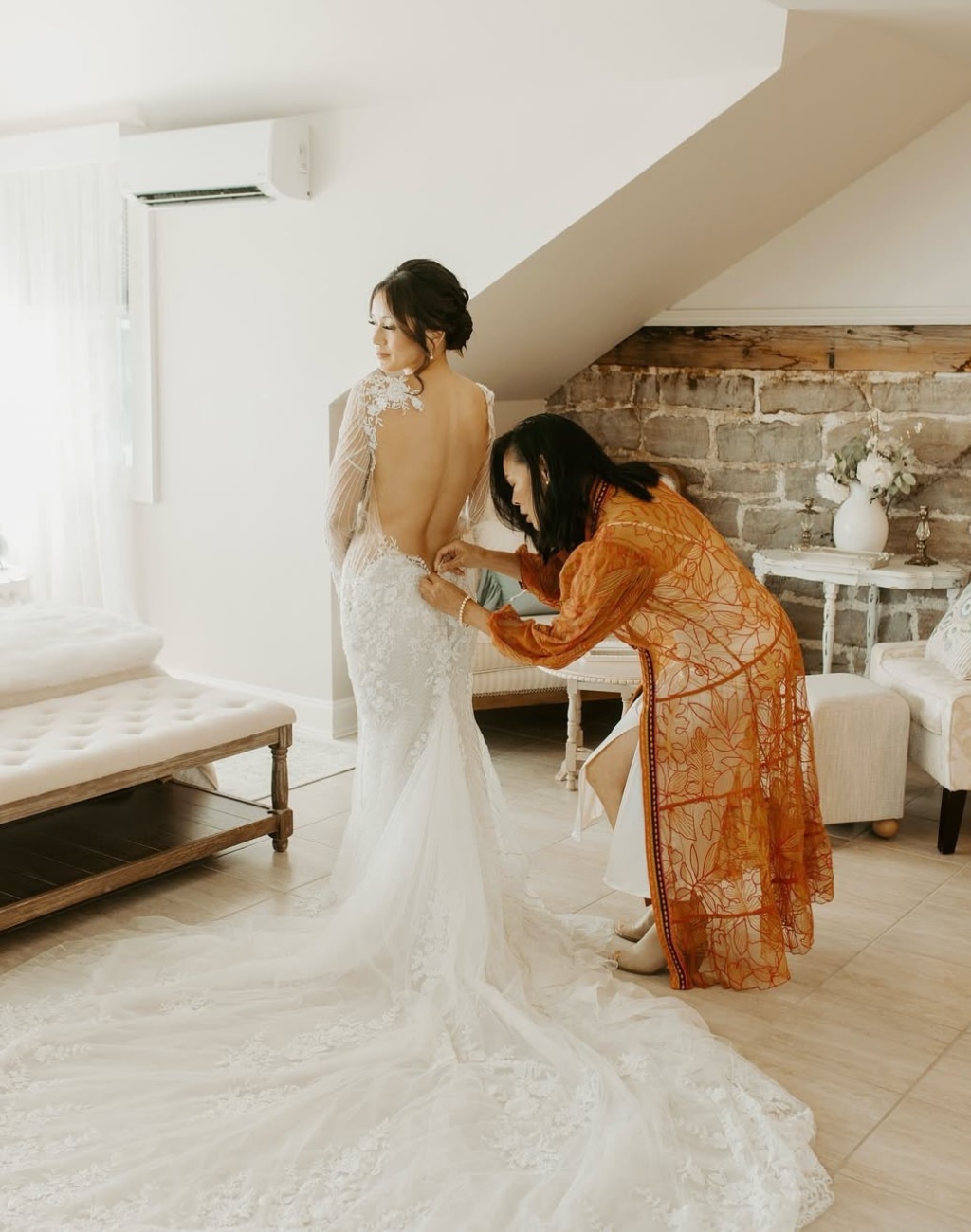 A beautiful photo of the mother of the bride zipping up the bride's wedding dress standing next to a big window