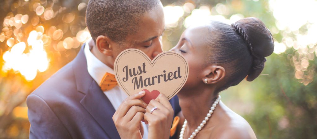 A bride and groom kissing holding up a wood sign that says just married