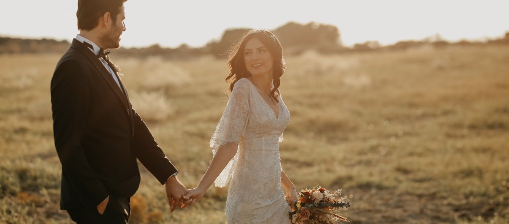 A bride and groom walking a field around sunset