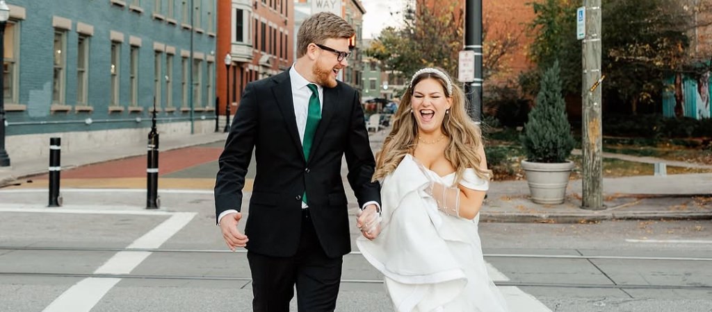 A bride and groom acting excited as they walk across a street