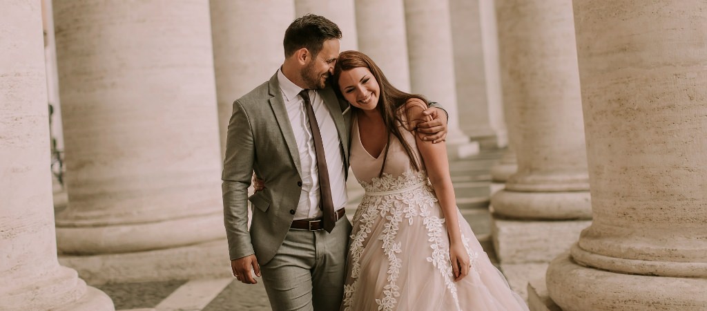 A bride and groom smiling and the guy has his arm around the girl