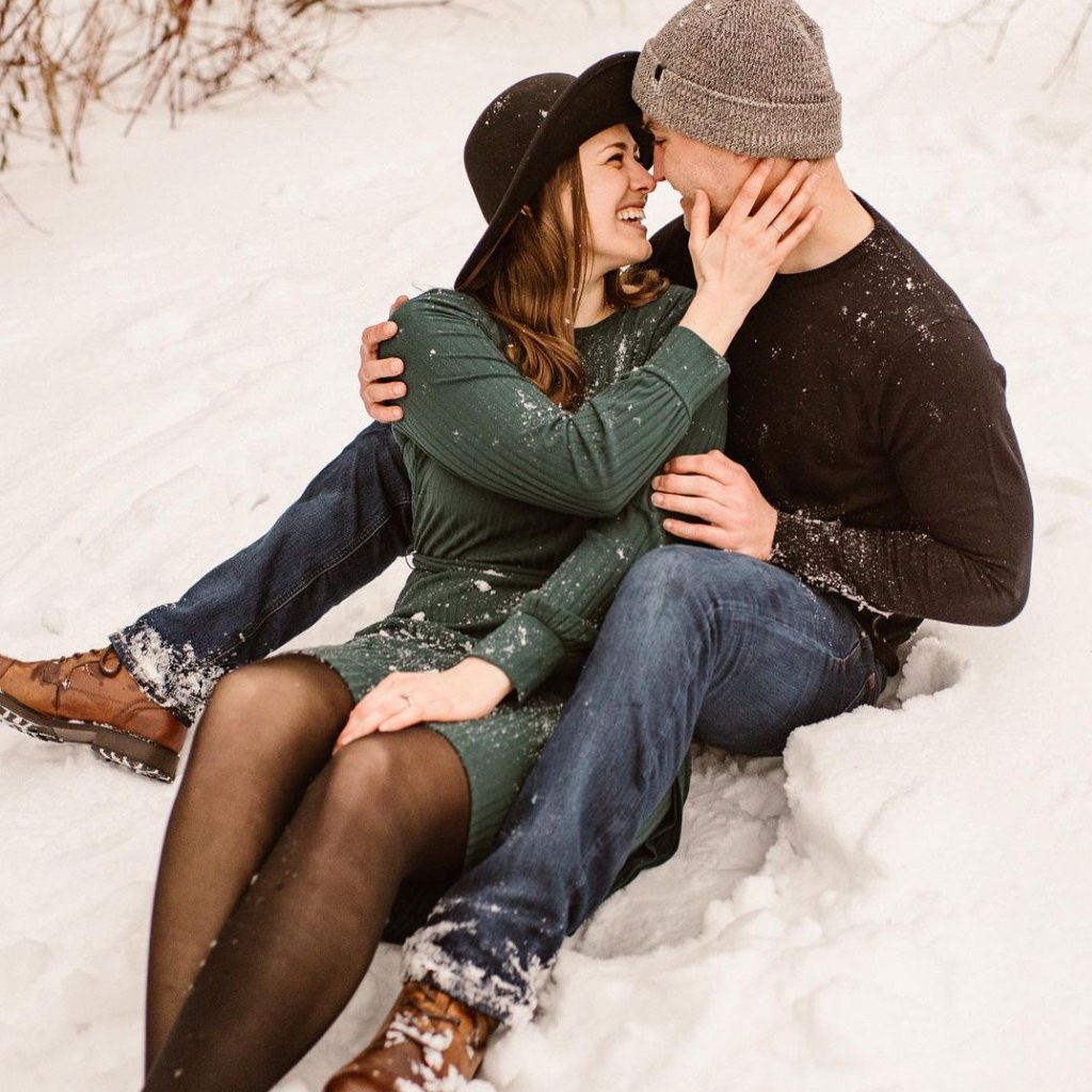 A couple sitting in the snow and taking engagement photos