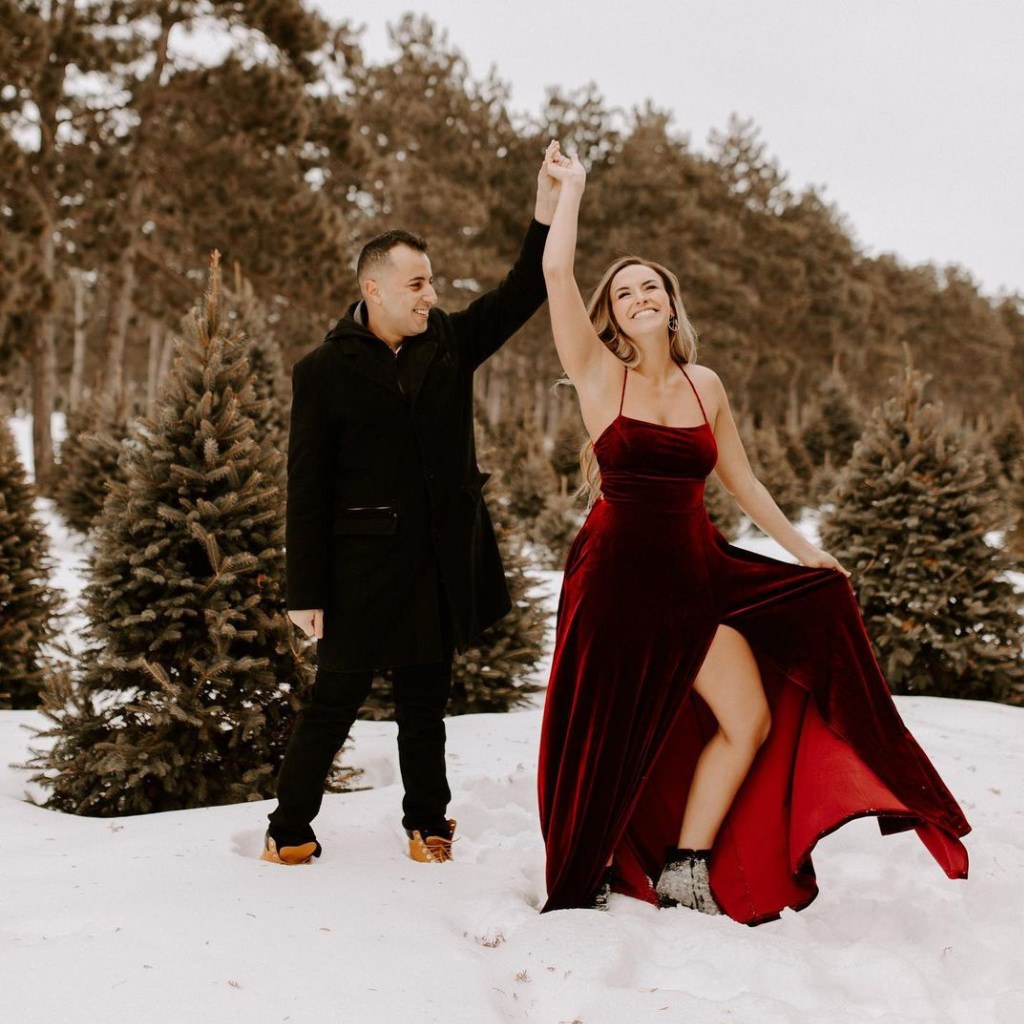 A girl wearing a bright red dress and a guy wearing all black. They are taking snow engagement photos in winter