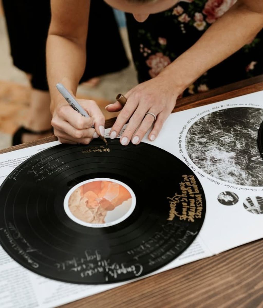 A wedding guest signing an old vinyl record that the couple is using for their wedding guest book alternative.