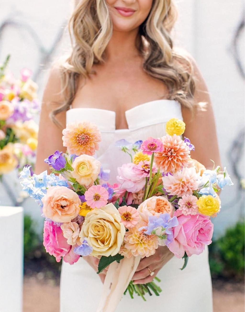 A close up photo of a spring wedding bouquet that has a mix of pink, yellow, lavender, and peach flowers