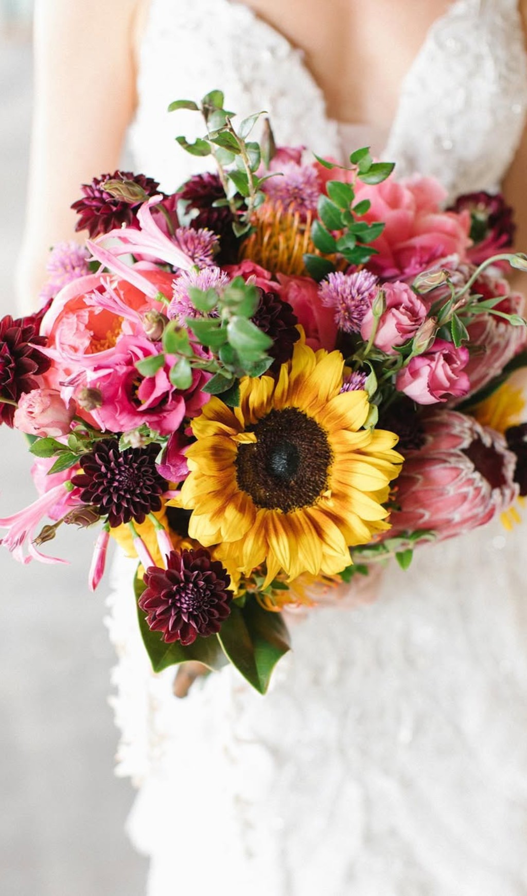 A beautiful summer wedding bouquet being held by the bride. This bouquet has lots of colors with a big sunflower in the middle