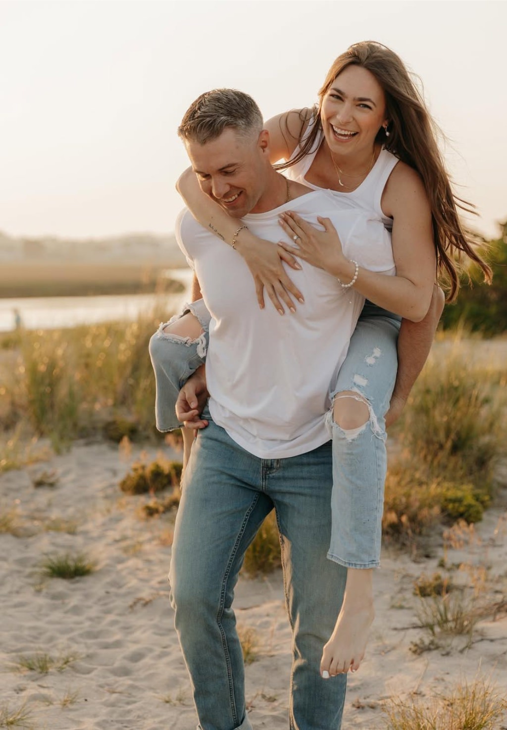 A playful couple posing for engagement photos in jeans and white tops