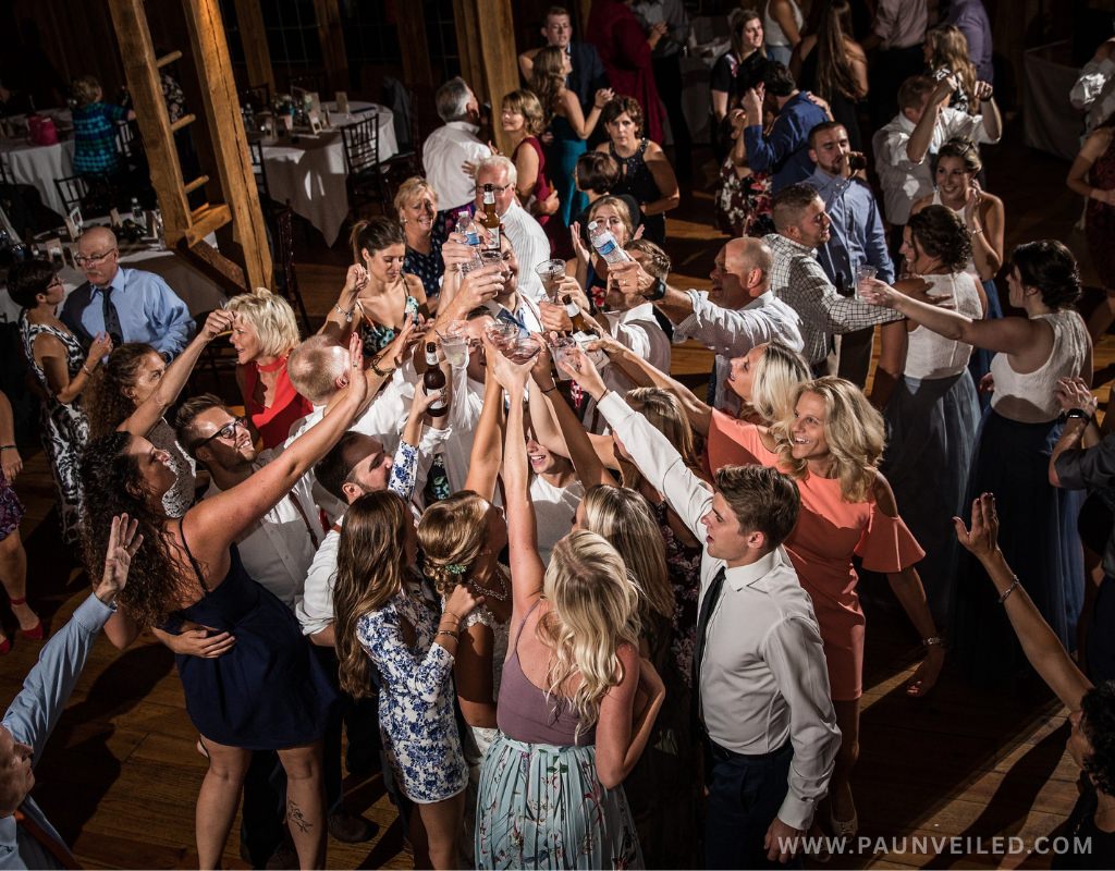 A group of adults having fun at a wedding reception with no kids and doing a cheers in the middle of the dance floor